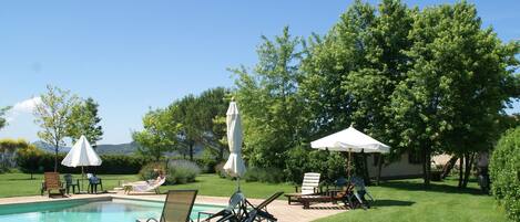 A poolside area with lounge chairs, umbrellas, and a clear view of the surrounding greenery and hills.