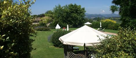 A gazebo with a white canopy, surrounded by lush greenery and a well-maintained lawn.