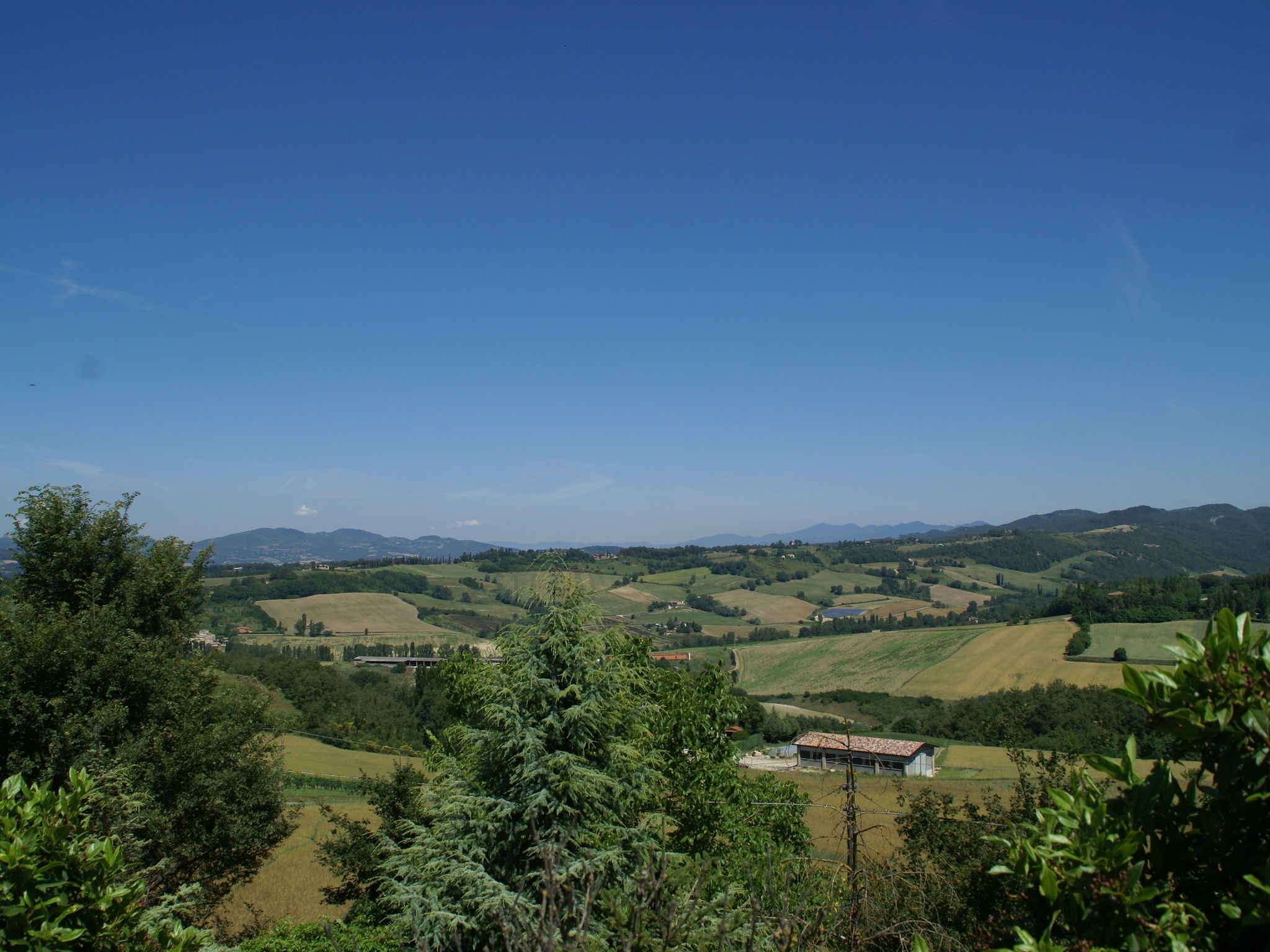 Un paysage rural avec des collines douces, un ciel bleu clair et un petit bâtiment doté d’un toit rouge.