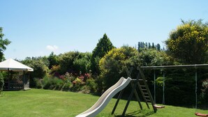 A grassy backyard with a slide, swing set, and a gazebo.