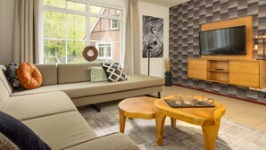 Ein Wohnzimmer mit Sofa, Couchtisch, Wandfernseher und einem fenster mit Vorhängen.