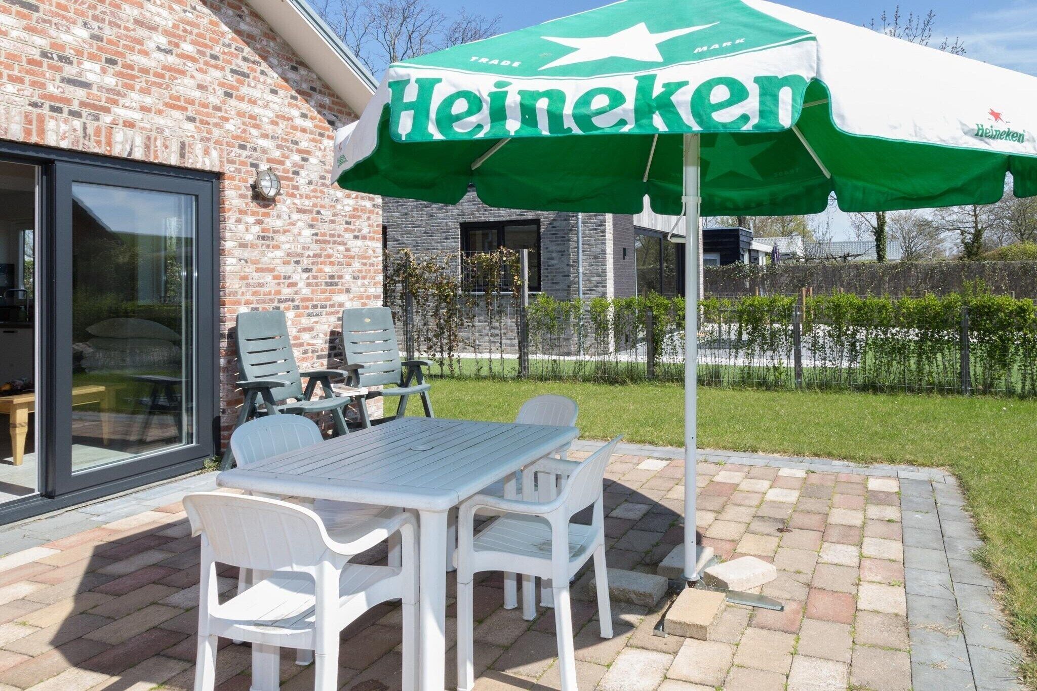Un patio con una mesa y sillas, una sombrilla de Heineken y un edificio de ladrillo al fondo.