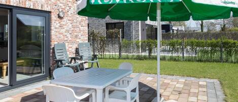 Un patio con una mesa y sillas, una sombrilla de Heineken y un edificio de ladrillo al fondo.