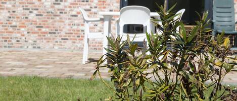 A brick building with a patio area, white plastic chairs, and a green lawn.