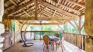 Un espace extérieur abrité, doté d’une terrasse en bois, de murs en pierre et d’un fauteuil suspendu.