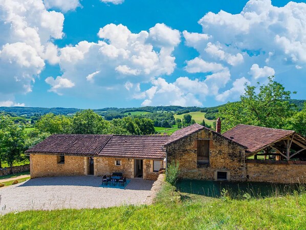 A stone building with a tiled roof, a gravel driveway, and a view of green hills and a blue sky with clouds. - Renovated farmhouse in Soturac with pool (Soturac)