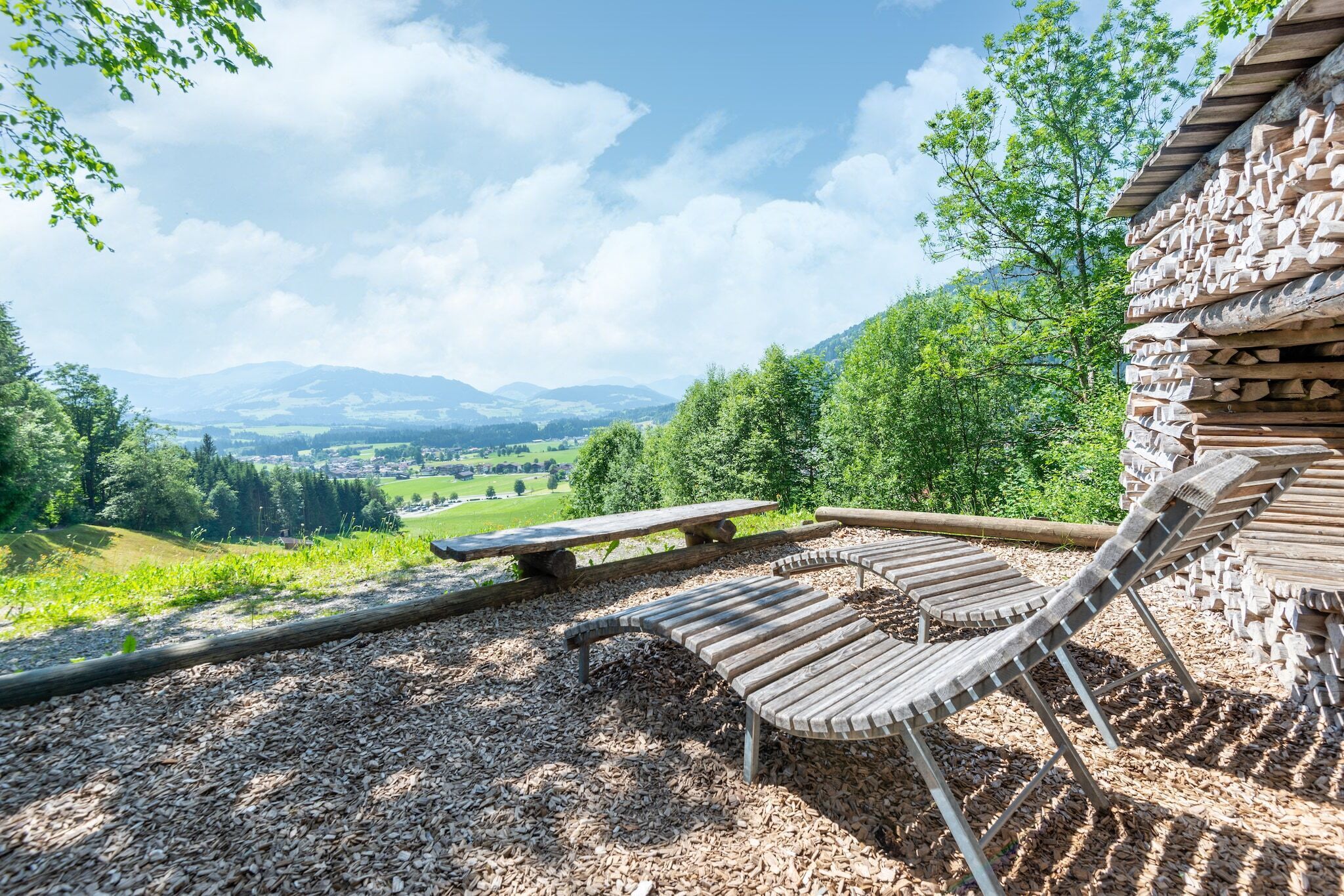 Une terrasse en bois, dotée de bancs et d’une table de pique-nique, offre une vue panoramique sur un paysage magnifique, avec des montagnes et une végétation luxuriante.