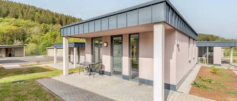 A modern building with a flat roof, large windows, and a paved patio area with outdoor seating.