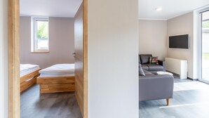 A modern room with a bed, a grey sofa, and a TV. - Komfortables Bungalow am Kronenburger See mit Terrasse (Hallschlag)