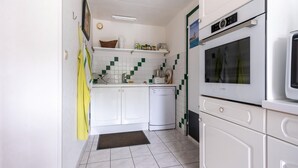 A compact kitchen with white cabinets, a dishwasher, and a built-in oven. - Stone-house cottage in Saussey with garden (Saussey)
