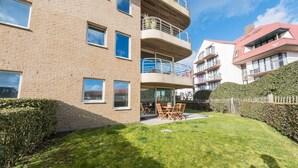 A multi-story residential building with a brick facade, balconies, and a small patio area with outdoor furniture. - Ground floor apartment with large garden (Middelkerke)