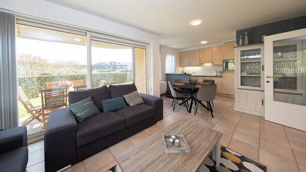 A modern living room with a sofa, coffee table, and dining area. - Ground floor apartment with large garden (Middelkerke)