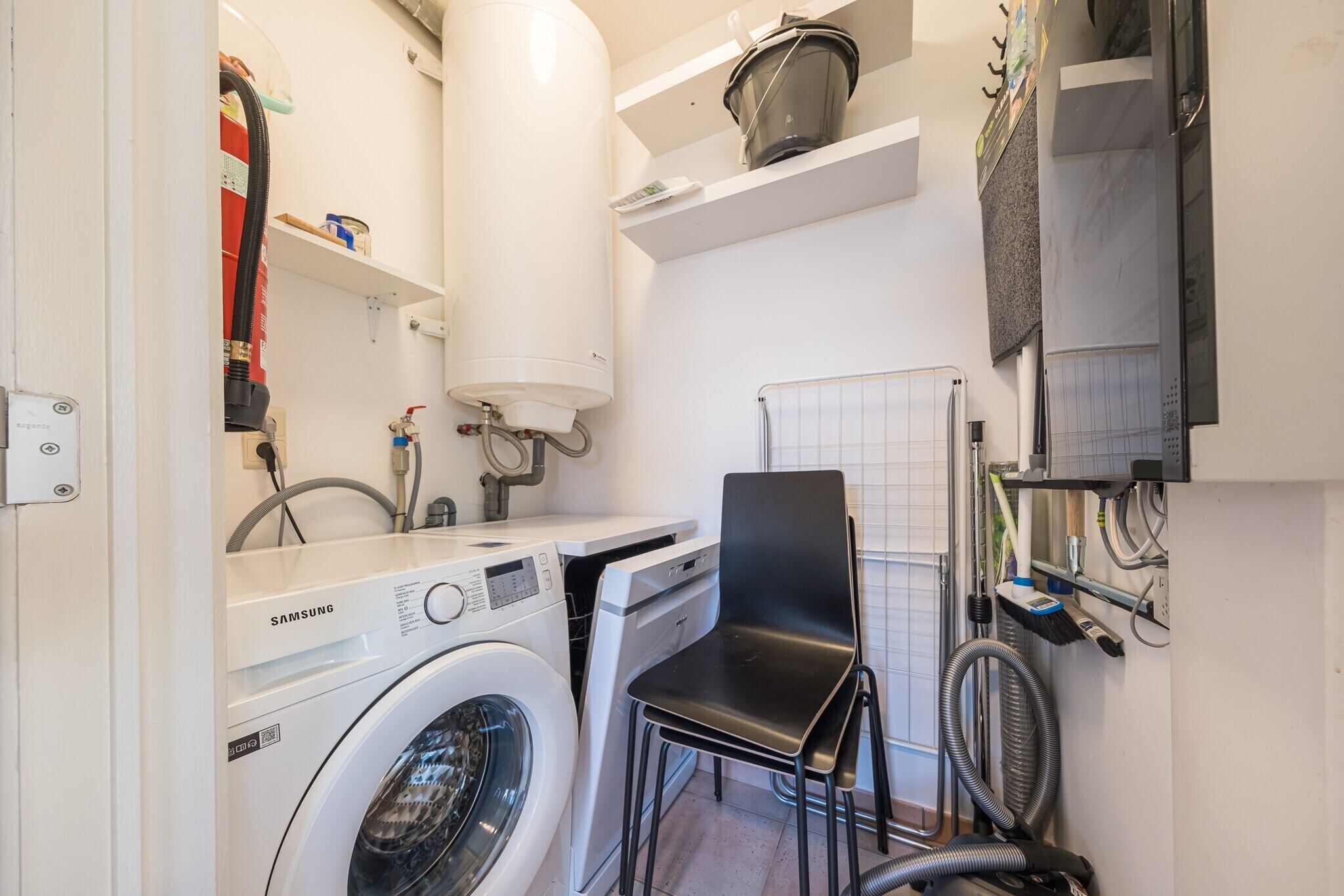 A laundry room with a Samsung washing machine, a dryer, a black chair, and a water heater.