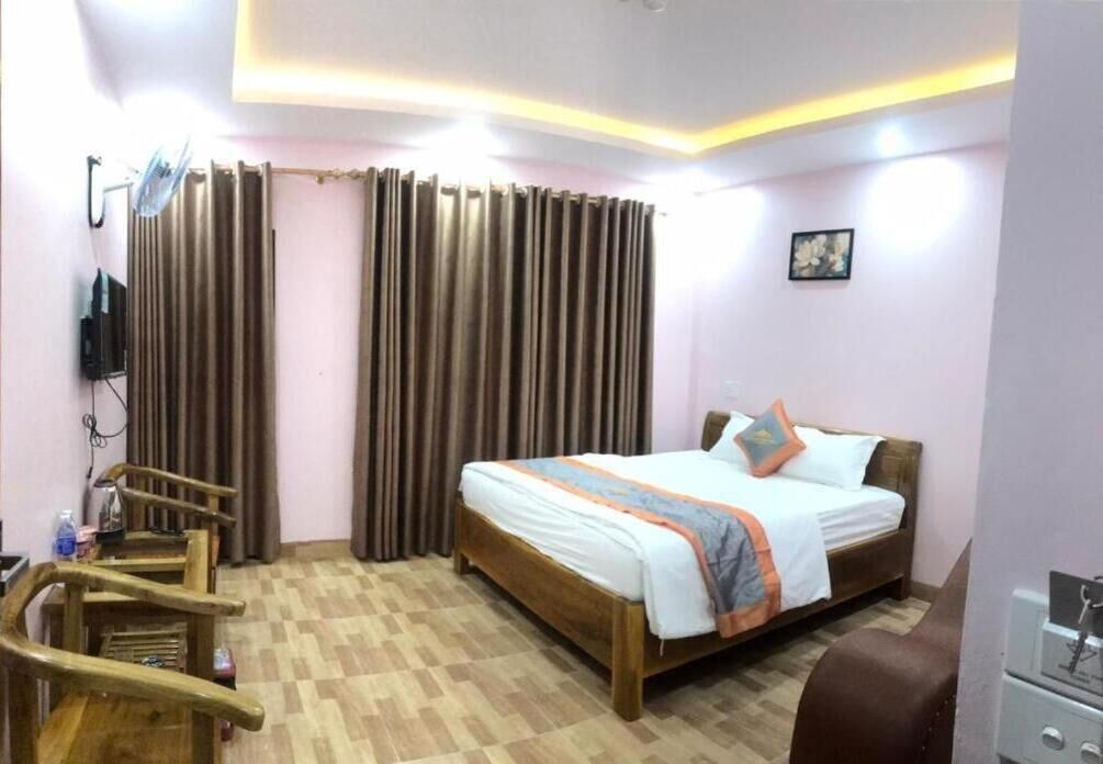 A hotel room with a wooden bed, a desk with a chair, a television, and curtains.