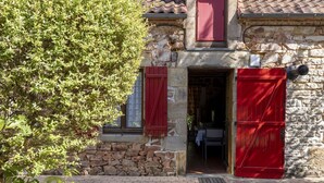 Un bâtiment en pierre avec des volets rouges, un escalier en pierre et une entrée pavée de briques.