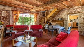 Un intérieur rustique en pierre, avec un coin repas, des canapés rouges et un escalier menant à un niveau supérieur.