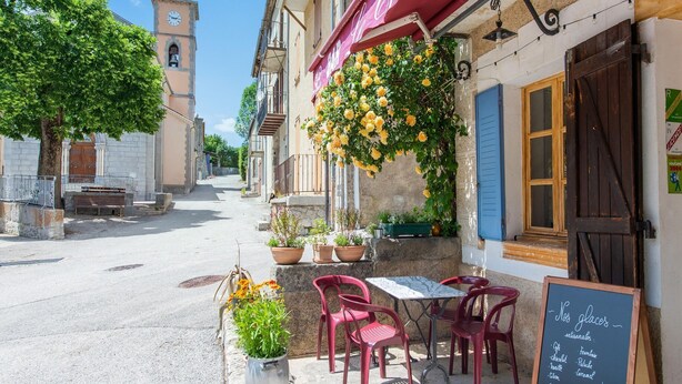 Una calle con un café que ofrece terraza, una iglesia al fondo y un cartel con los platos del menú.