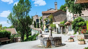 Una calle pintoresca en un pueblo con edificios de piedra, una torre del reloj y un coche estacionado en la vía.