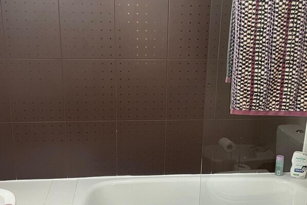 A bathroom with a white bathtub, a towel rack with patterned towels, and toiletries on the side.