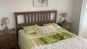 Un lit bien fait, avec une literie verte et blanche, deux tables de chevet avec des lampes et une œuvre d’art accrochée au mur.