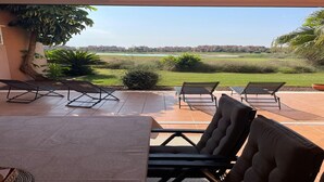 Une terrasse avec des sièges extérieurs, offrant une vue sur un paysage verdoyant et des bâtiments situés au loin.