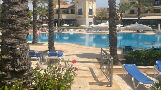 Un espace piscine avec des chaises longues, des palmiers et un bâtiment doté de balcons.