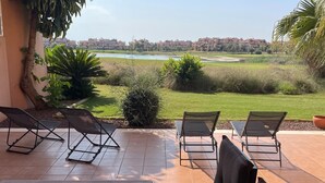 Une terrasse avec quatre chaises longues et une table, offrant une vue sur un terrain de golf et des immeubles résidentiels.