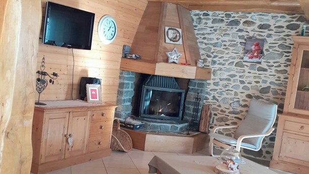 L’intérieur chaleureux d’un chalet avec un mur en pierre, des meubles en bois, une cheminée et un téléviseur fixé au mur.