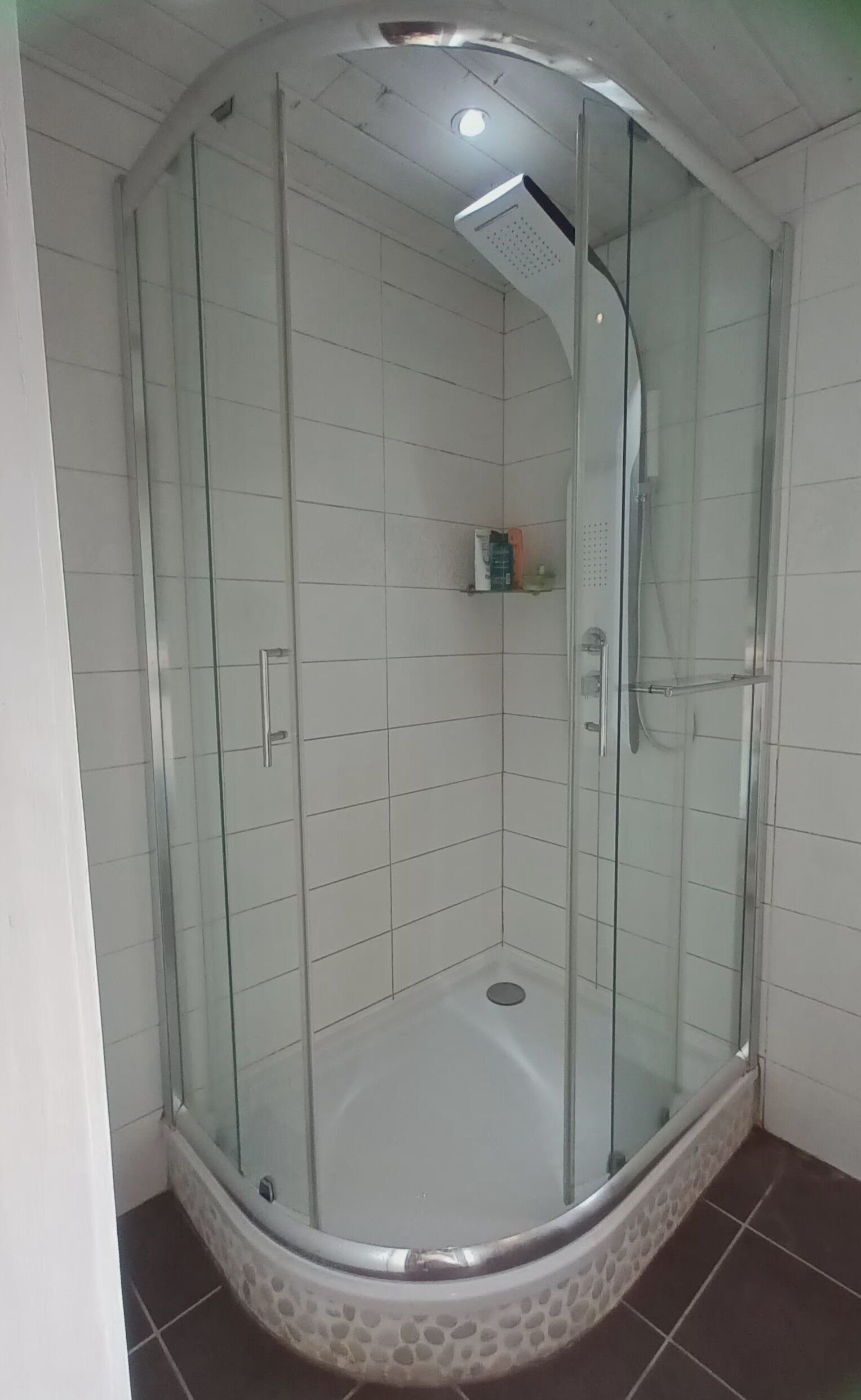 A glass-enclosed shower stall with a white tiled floor and a curved ceiling.