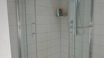 Un box de ducha con paredes de vidrio, piso de baldosas blancas y techo curvo.