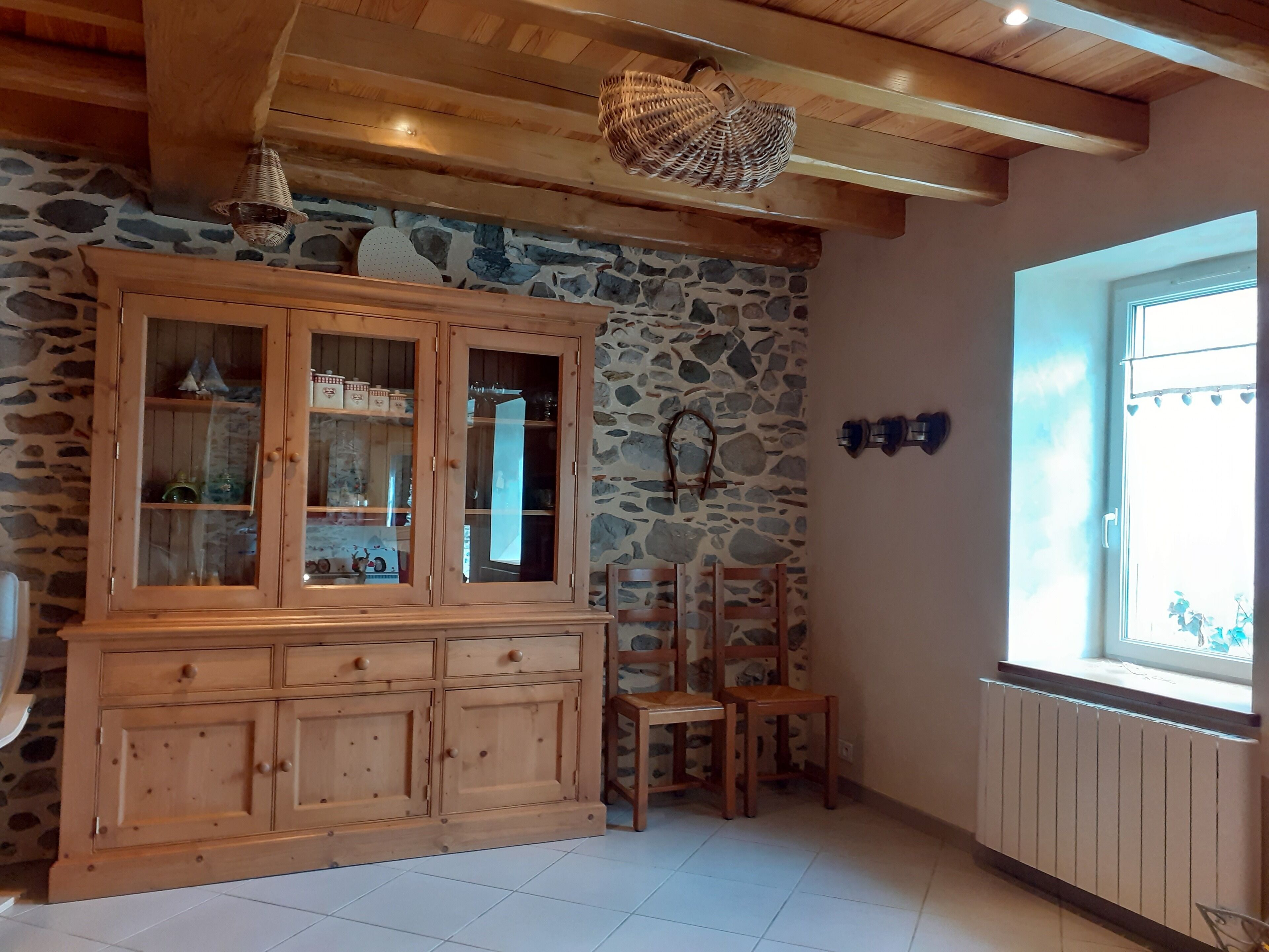 A wooden cabinet with glass doors, a stone wall, and a window with curtains.