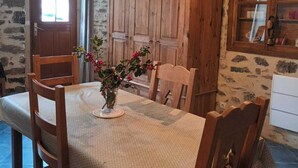 Un coin repas rustique avec une table en bois, des chaises et un vase rempli de fleurs. Des luminaires sont suspendus au-dessus de la table.
