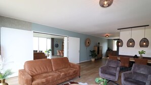 A living room with a sofa, armchairs, a coffee table, and a dining area with chairs and a table.