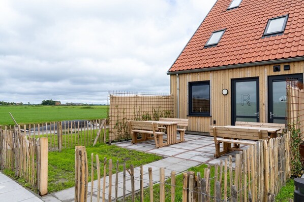 A wooden building with a tiled roof, a fenced outdoor area with a bench, and a paved patio.
