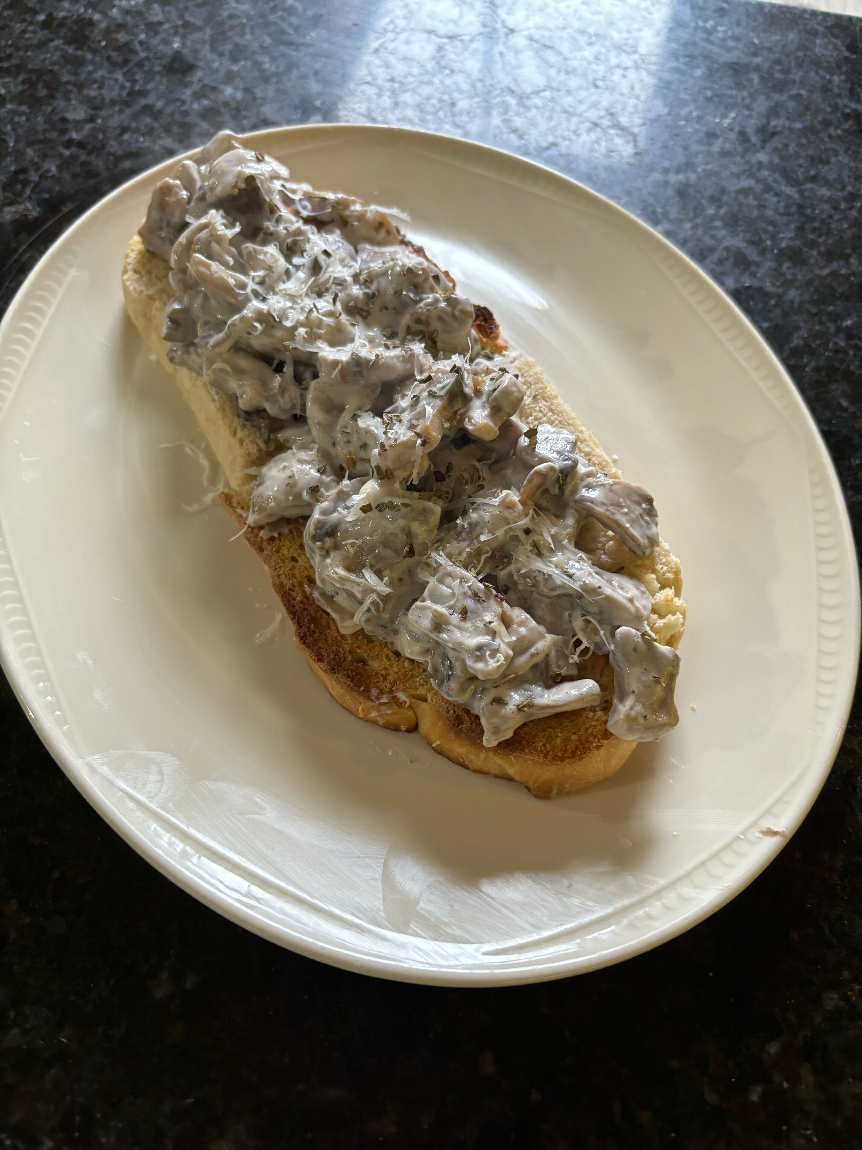 Un plato blanco con un sándwich sobre una encimera oscura.