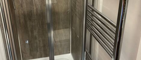 Une cabine de douche fermée par des parois en verre, dotée d’une étagère intégrée pour ranger les articles de toilette.