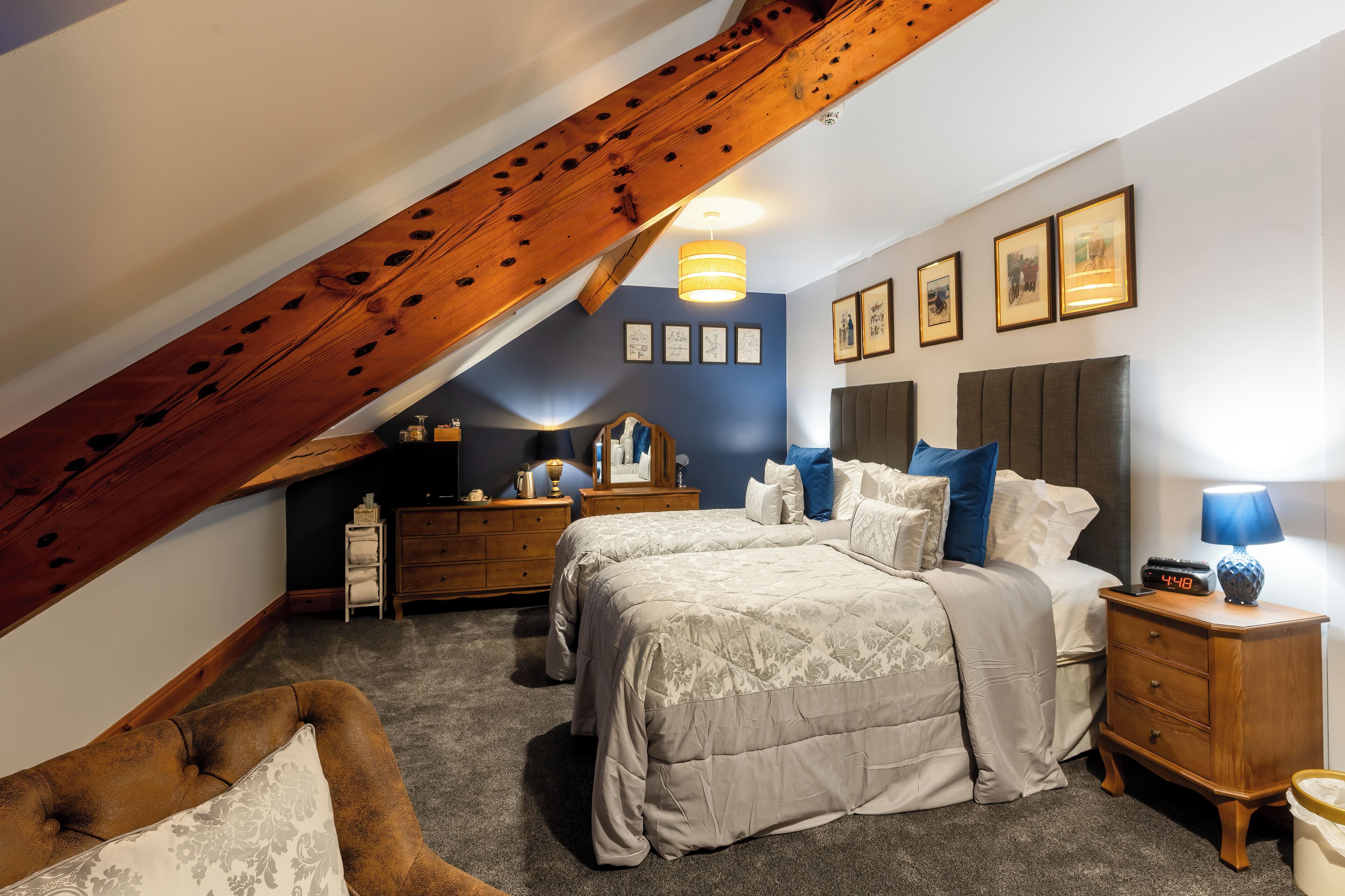 A bedroom with two beds, a wooden ceiling beam, a dresser, a nightstand, and a lamp.