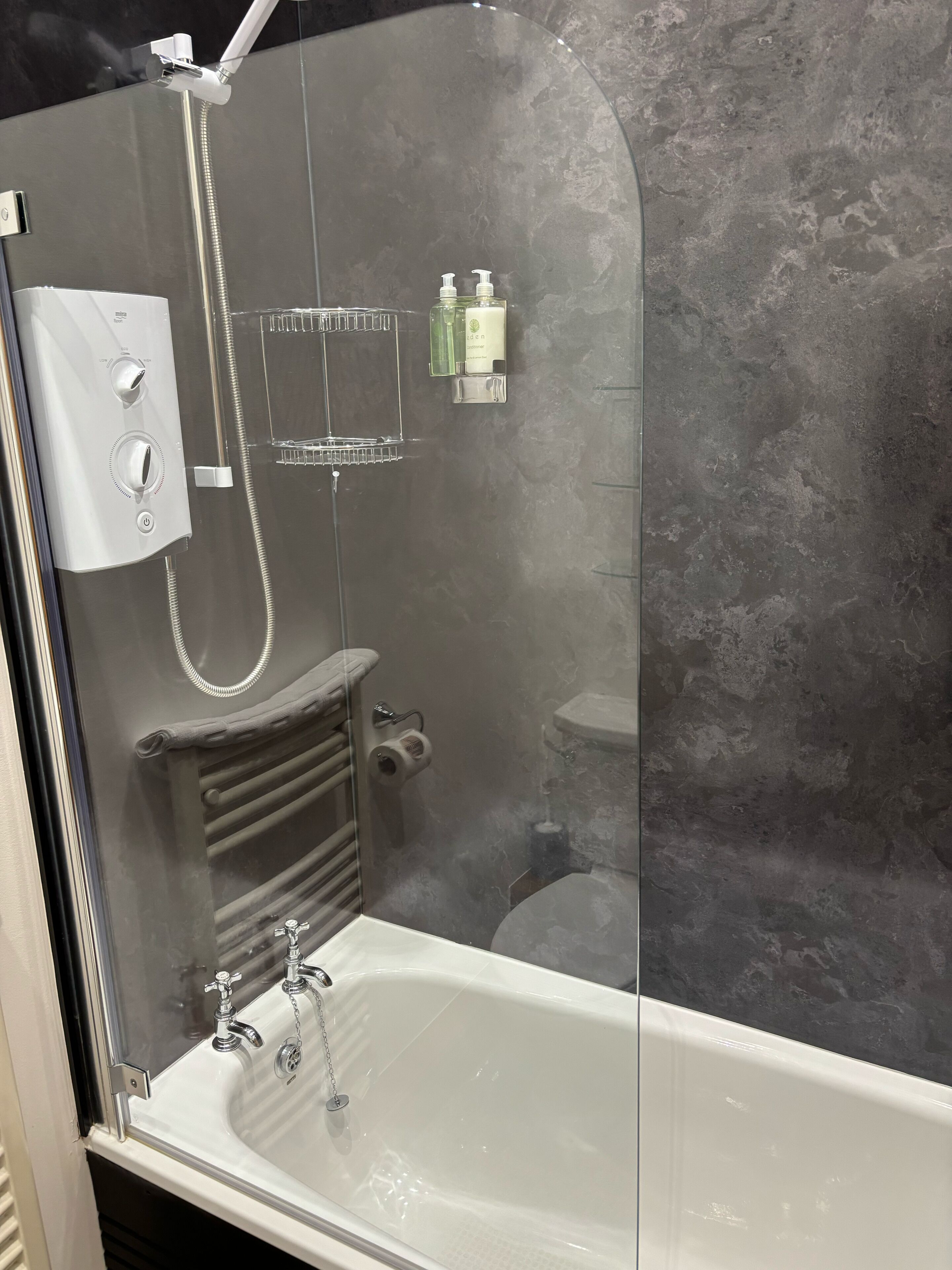 Une salle de bain moderne avec une douche à parois de verre, une baignoire blanche et un mur gris à texture.