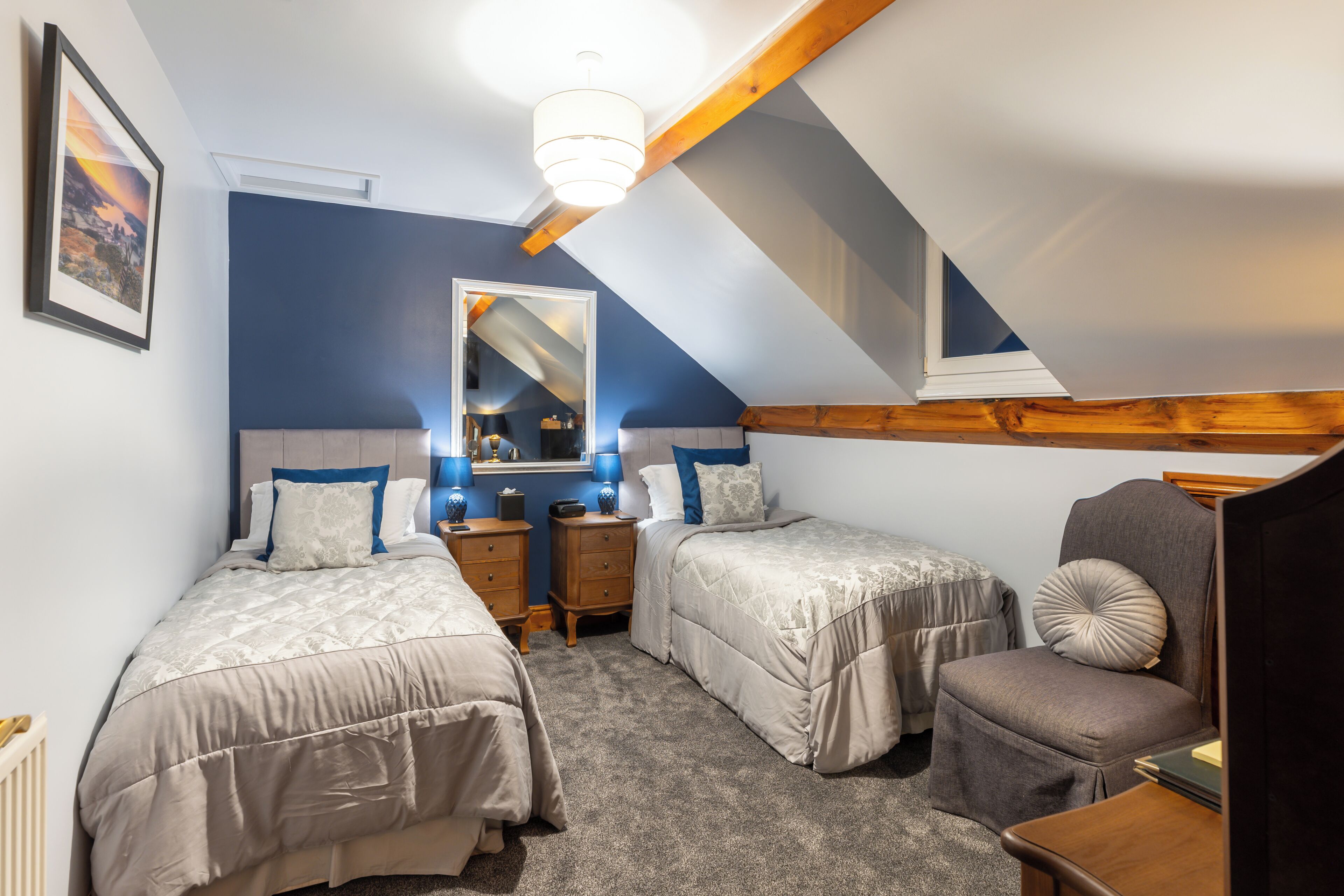 A bedroom with two beds, a chair, a nightstand, a mirror, and a ceiling light.