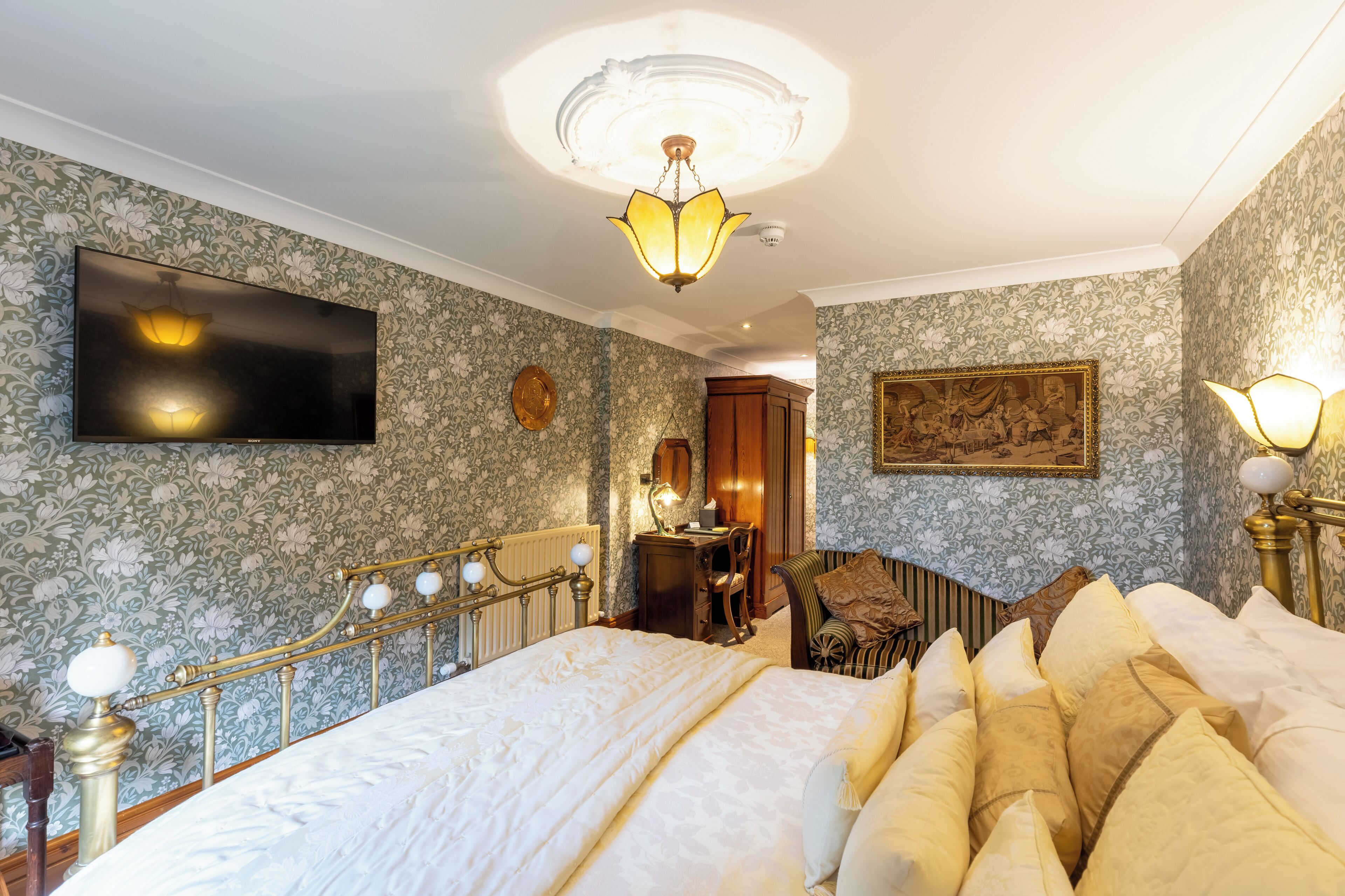 A bedroom with a large bed, a desk, a chair, and a television on the wall.