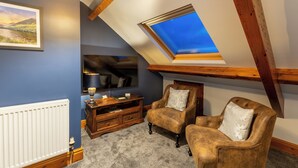 A room with a sloped ceiling, a skylight, a white radiator, a wooden cabinet, and two leather armchairs with cushions. - Brooklands Guest House  (Penrith)