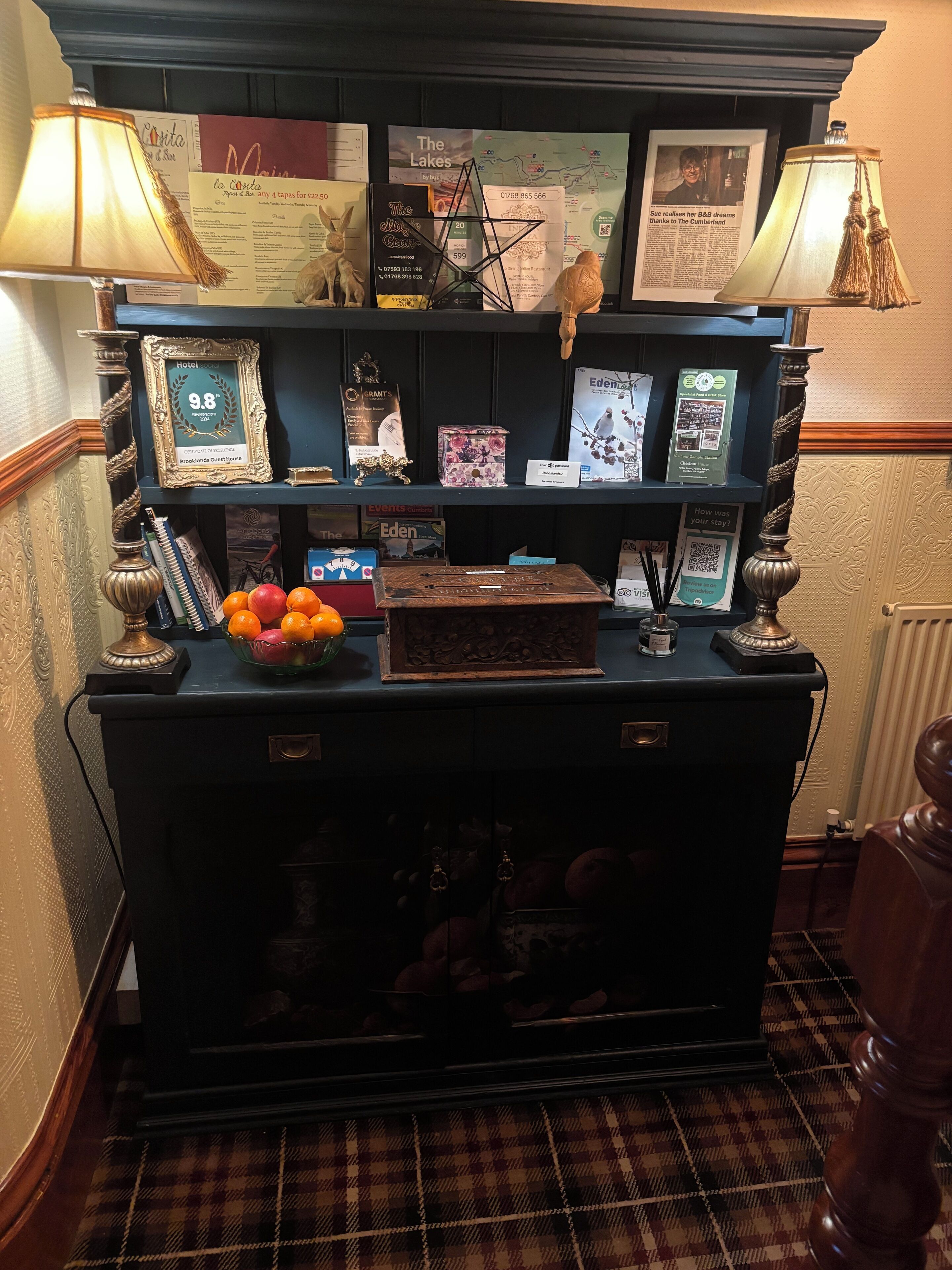 A reception desk with a framed certificate of excellence, a decorative lamp, a bowl of fruit, and various informational brochures.