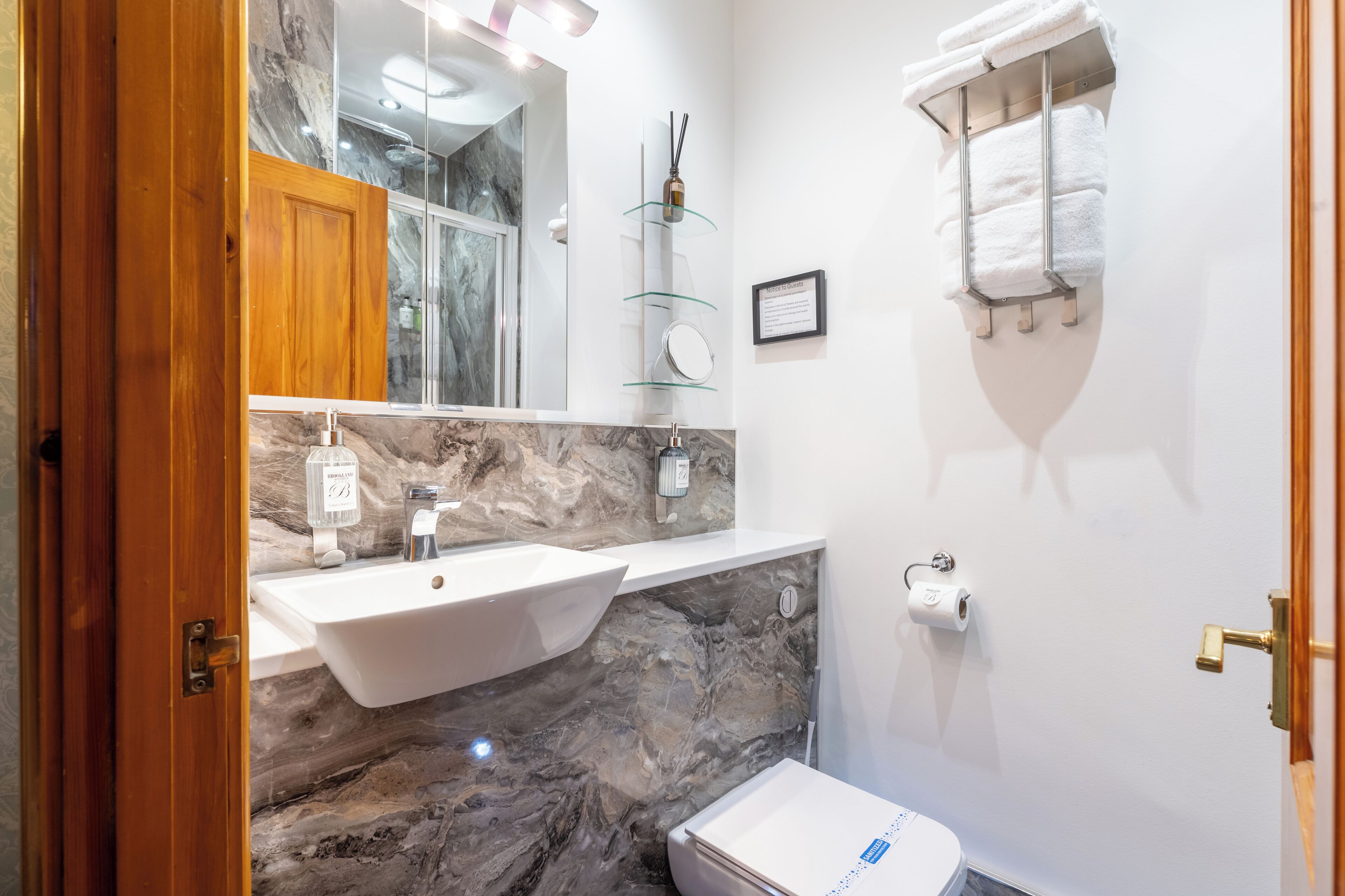 Ein Badezimmer mit Marmorwaschbecken, Toilette, Handtuchhalter und Ablage aus Glas.