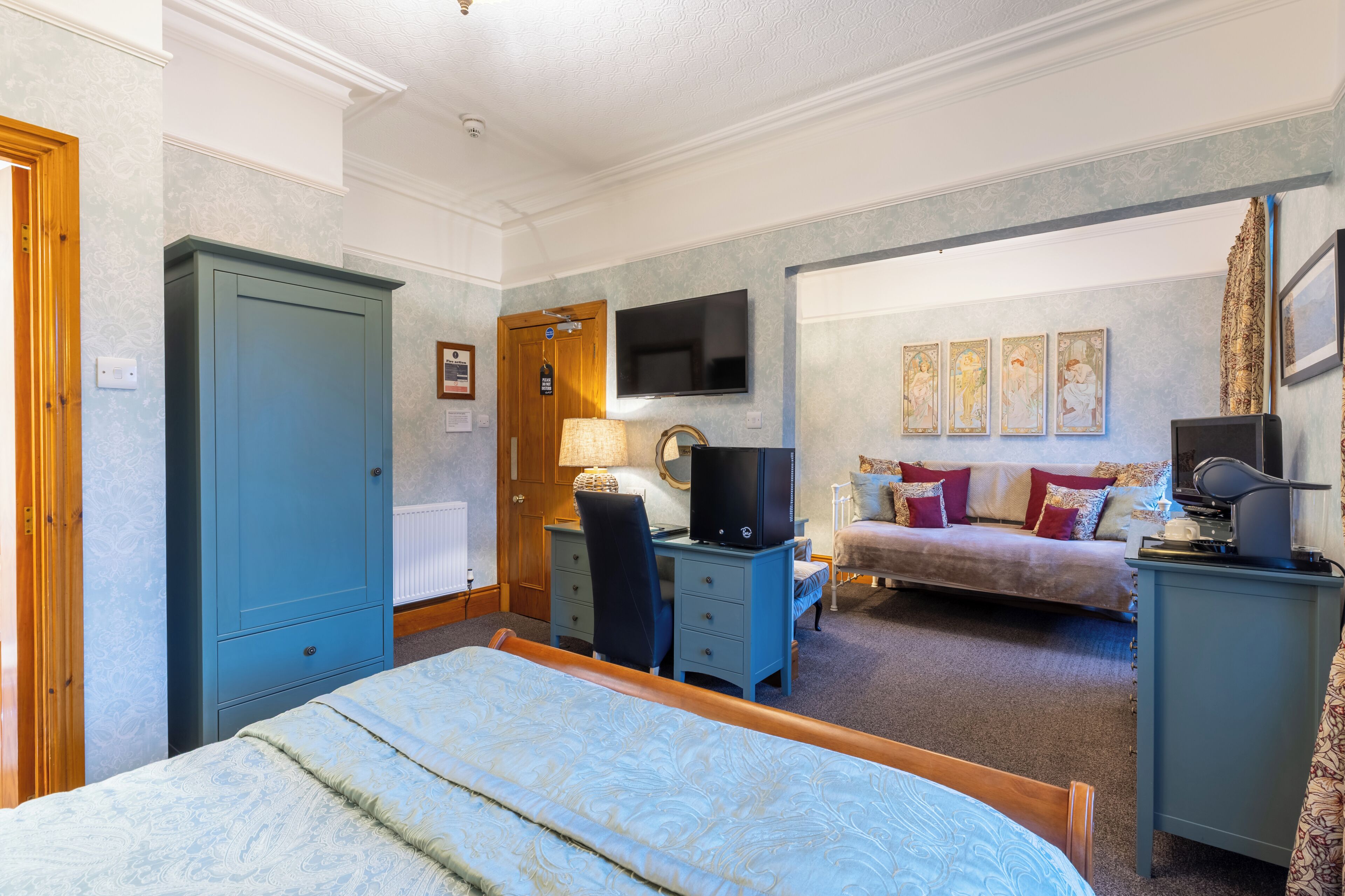 A bedroom with a bed, a desk, a TV, and a sofa.