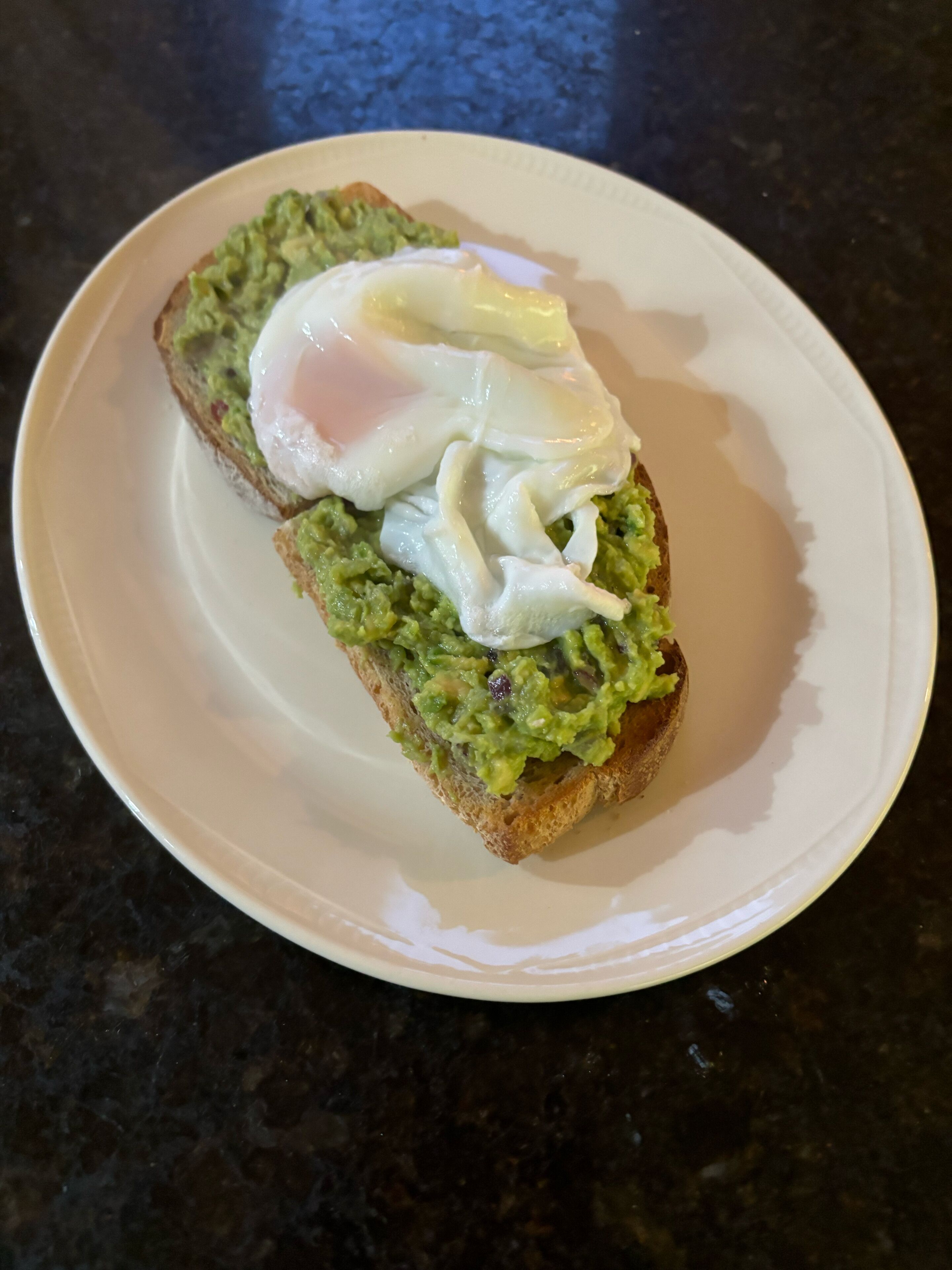 Une assiette avec un sandwich posé sur un comptoir foncé.