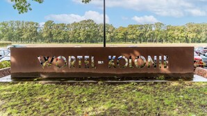 A sign with the text "VORIL-KOLONI" in a metal structure, surrounded by grass and trees.