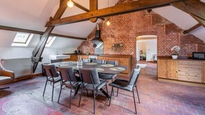 Un loft amplio con vigas de madera expuestas, cocina de ladrillo y comedor con una mesa redonda y sillas.