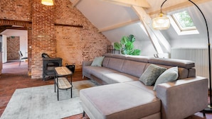 Un espacio tipo loft con paredes de ladrillo visto, un sofá grande, una mesa de madera y una lámpara colgante.