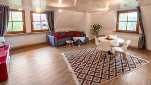 A spacious living room with a gray sofa, red cushions, a glass coffee table, and a patterned rug. - Elegante Ferienwohnung mit Außenpool Schwarzwald (Herrischried)