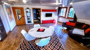 A modern living room with a round dining table, white chairs, a black sofa, and a red cabinet. - Elegante Ferienwohnung mit Außenpool Schwarzwald (Herrischried)